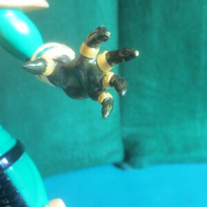 Op de afbeelding: Een groene actiefiguurhand met donkergroene vingers en puntige uiteinden, voorzien van gouden bandjes rond elke vinger en de pols. De hand is uitgestrekt en bevestigd aan een groene arm met een zwarte band en een gouden schouderstuk.