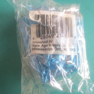 Puede incluir: Una bolsa de pl&aacute;stico transparente que contiene un objeto azul. Una etiqueta blanca con un c&oacute;digo de barras y texto es visible. El texto incluye "Importado por: New Age Supply Co. Mississauga, Ont. 14V 1R3".