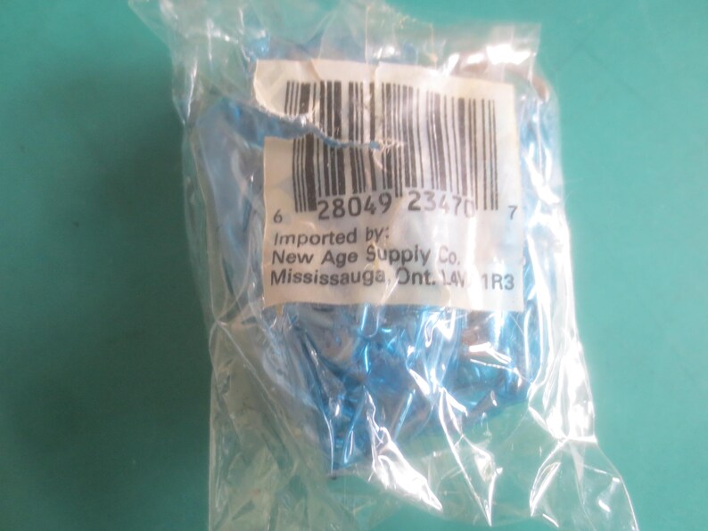 Puede incluir: Una bolsa de pl&aacute;stico transparente que contiene un objeto azul. Una etiqueta blanca con un c&oacute;digo de barras y texto es visible. El texto incluye "Importado por: New Age Supply Co. Mississauga, Ont. 14V 1R3".