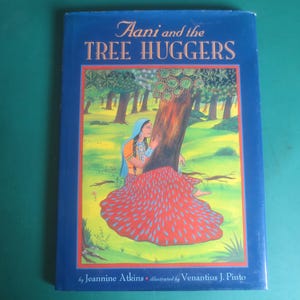 May include: A blue hardcover book titled "Aani and the Tree Huggers" with an illustration of a woman hugging a tree. The illustration features a woman in a red skirt and a blue head covering. The book is by Jeannine Atkins and illustrated by Venantius J. Pinto.