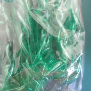 Puede incluir: Primer plano de una bolsa de pl&aacute;stico transparente llena de m&uacute;ltiples objetos verdes. Los objetos son de un tono verde vibrante y parecen estar hechos de un material brillante. La bolsa es parcialmente transparente, lo que permite vislumbrar el contenido.