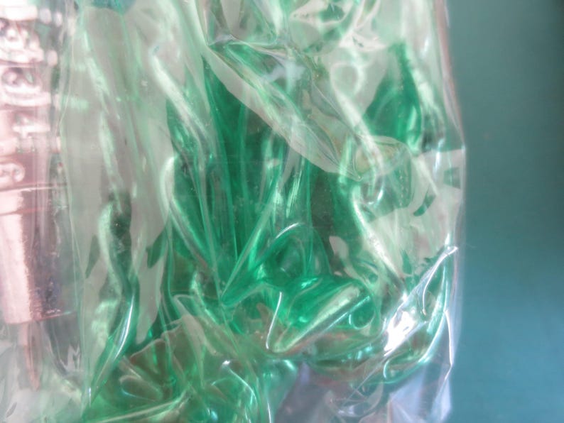 Puede incluir: Primer plano de una bolsa de pl&aacute;stico transparente llena de m&uacute;ltiples objetos verdes. Los objetos son de un tono verde vibrante y parecen estar hechos de un material brillante. La bolsa es parcialmente transparente, lo que permite vislumbrar el contenido.