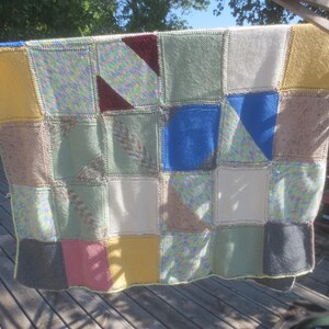 May include: A handmade knit blanket composed of various square patches in multiple colors including yellow, blue, green, pink, white, and grey. Some squares feature solid colors while others display variegated yarn patterns or diagonal color-blocked designs.