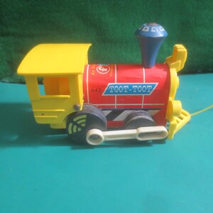 May include: A vintage toy train with a yellow cab and accents, a red body with the words "TOOT-TOOT", and a blue smokestack. The train has black wheels and a yellow pull string. The toy is made of plastic.