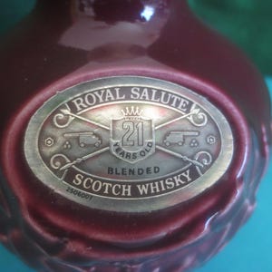 May include: A maroon-colored bottle with a silver label that reads "Royal Salute 21 Years Old Blended Scotch Whisky." The label features a crown, cannons, and the text "2506007."