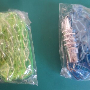 Puede incluir: Dos bolsas de pl&aacute;stico selladas. Una contiene una cadena verde, la otra una cadena azul. Un candado de combinaci&oacute;n plateado es visible en la bolsa de cadena azul. Las cadenas son probablemente para la fabricaci&oacute;n de joyas o manualidades.