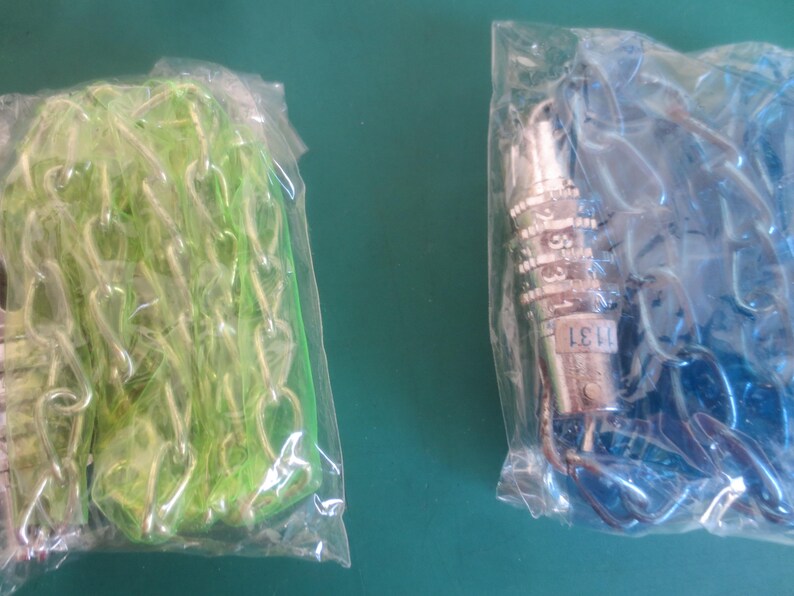 Puede incluir: Dos bolsas de pl&aacute;stico selladas. Una contiene una cadena verde, la otra una cadena azul. Un candado de combinaci&oacute;n plateado es visible en la bolsa de cadena azul. Las cadenas son probablemente para la fabricaci&oacute;n de joyas o manualidades.