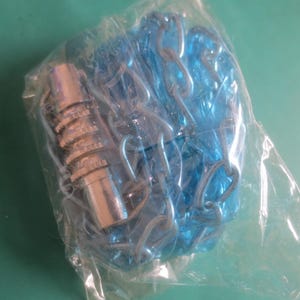 Puede incluir: Un paquete que contiene un objeto met&aacute;lico plateado y una cadena de pl&aacute;stico azul. El objeto met&aacute;lico tiene un dise&ntilde;o estriado. La cadena est&aacute; hecha de anillos enlazados. Los art&iacute;culos est&aacute;n encerrados en una bolsa de pl&aacute;stico transparente.