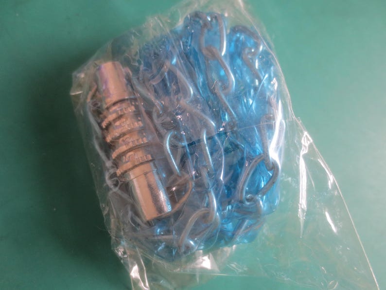 Puede incluir: Un paquete que contiene un objeto met&aacute;lico plateado y una cadena de pl&aacute;stico azul. El objeto met&aacute;lico tiene un dise&ntilde;o estriado. La cadena est&aacute; hecha de anillos enlazados. Los art&iacute;culos est&aacute;n encerrados en una bolsa de pl&aacute;stico transparente.