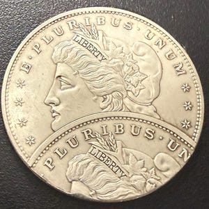 Può includere: Una moneta d'argento raffigurante il profilo di una donna con capelli fluenti, circondata dalle iscrizioni "E PLURIBUS UNUM" e "LIBERTY". La moneta presenta un design dettagliato con stelle e spighe di grano.