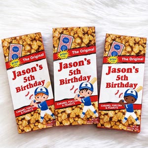 May include: Three boxes of caramel popcorn and peanuts for a 5th birthday. Each box features a baseball theme with a cartoon boy in a baseball uniform, a baseball bat, and the text "Jason's 5th Birthday". The boxes are filled with popcorn.