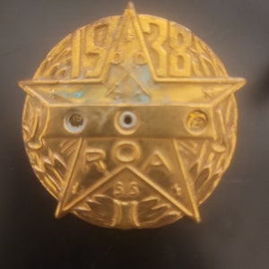 May include: A gold-colored metal star-shaped pin with the text "1928 ROA 35" and a wreath design around the star.