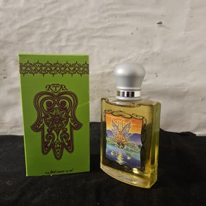 May include: A perfume bottle with a silver cap and a green box. The bottle has a colorful illustration of a fairy. The box has a hand symbol and the letters KTR. The bottle contains 25 ml of fluid.