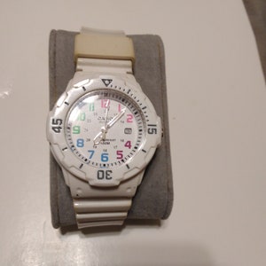 May include: White wristwatch with a white band and a white face. The face has black numbers and a black bezel. The watch is water resistant to 100 meters.