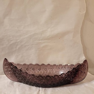 May include: A purple glass serving dish shaped like a boat with a scalloped edge and a floral pattern.