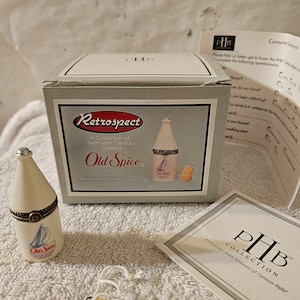 May include: A white porcelain bottle with a gold lid and a label that reads "Old Spice After Shave Cologne". The bottle is in a white box with the words "Retrospect" and "Old Spice" on it. The box is part of a collection of twentieth-century classics.