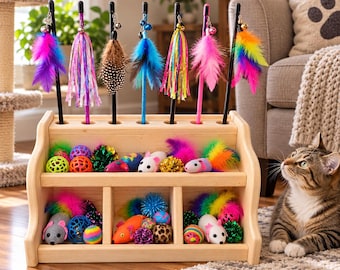 May include: A light-colored wooden storage rack with two shelves holding various cat toys, including plush mice, textured balls, and colorful pom-poms. Seven cat wand toys with feathers, ribbons, and bells are inserted into holes along the top.