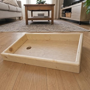 May include: A rectangular wooden tray with light-colored natural wood grain, featuring four raised sides and a flat base. A single circular hole is cut into the bottom surface of the tray, positioned toward the left side of the structure.