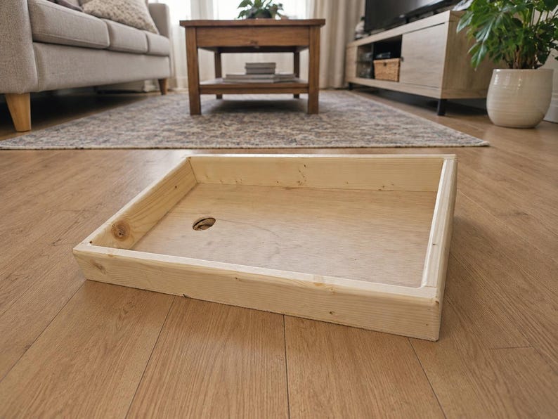 May include: A rectangular wooden tray with light-colored natural wood grain, featuring four raised sides and a flat base. A single circular hole is cut into the bottom surface of the tray, positioned toward the left side of the structure.
