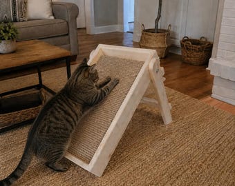 May include: A brown tabby cat stretches its front paws onto an adjustable, light-colored wooden cat scratching ramp. The ramp features a textured, tan-colored sisal scratching surface set within a sturdy, rectangular wooden frame.