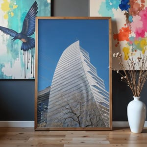 Peut inclure: Photographie encadrée d'un gratte-ciel blanc moderne se détachant sur un ciel bleu clair. Le bâtiment présente un design incurvé unique avec de nombreuses fenêtres. Le cadre est de couleur marron clair et chaleureux. Un arbre est devant le bâtiment.