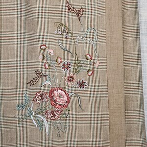 Può includere: Primo piano di un tessuto a quadri beige con ricami floreali. Il ricamo presenta fiori rosa, rossi e verdi. Un pannello verticale beige è visibile sul lato destro.
