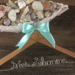 May include: Wooden hanger with a teal bow and the text "Erin & Sherbel 9.25.18" engraved on the hanger. A silver wire inscription reads "Mrs. Shanine".