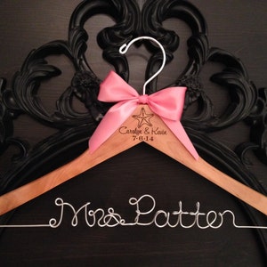 May include: Wooden hanger with a pink bow and the text "Carolyn & Kevin 7-0-14" engraved on the top. The hanger has a silver wire inscription that reads "Mrs. Patten".