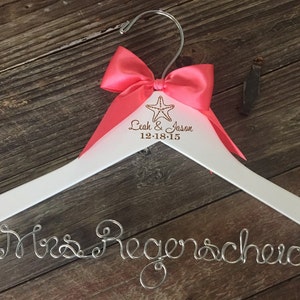 May include: White wooden hanger with a pink bow and the text "Leah & Jason 12-18-15" and a starfish. The hanger has a silver wire inscription that says "Mrs. Regenscheid".