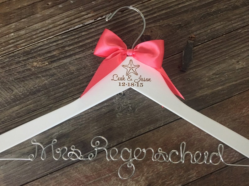 May include: White wooden hanger with a pink bow and the text "Leah & Jason 12-18-15" and a starfish. The hanger has a silver wire inscription that says "Mrs. Regenscheid".