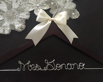 May include: A brown wooden hanger with a white satin bow and a silver wire inscription that reads "Mrs. Donano".