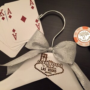 May include: A white wooden hanger with a silver bow and a Las Vegas sign that says "Welcome to Fabulous Las Vegas Nevada". There are playing cards and casino chips on the table.