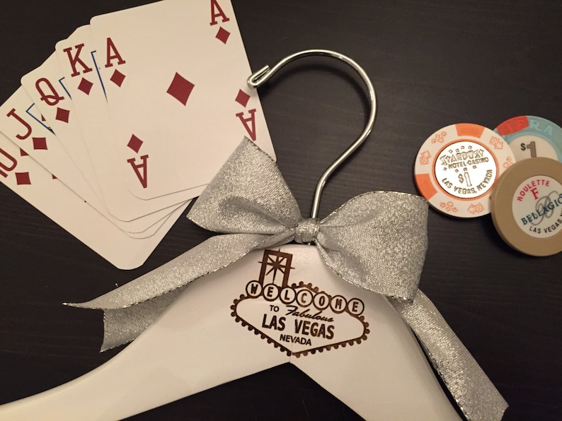 May include: A white wooden hanger with a silver bow and a Las Vegas sign that says "Welcome to Fabulous Las Vegas Nevada". There are playing cards and casino chips on the table.