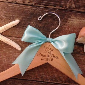 May include: A wooden hanger with a light blue satin bow and a starfish design. The hanger is personalized with the text "Erica & Gary 5-12-12".