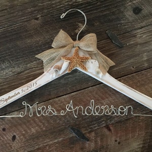 May include: A white wooden hanger with a burlap bow, starfish, and seashells. The wire reads "Mrs. Anderson". The date "September 5, 2015" is engraved on the hanger.