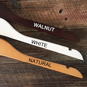 May include: Three wooden hangers in different colors: walnut, white, and natural. The hangers are labeled with their respective colors.