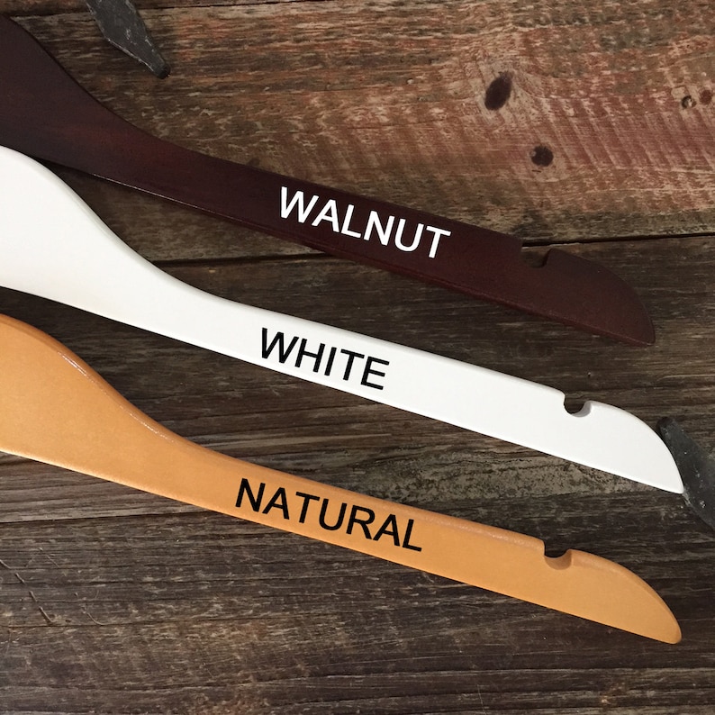 May include: Three wooden hangers in different colors: walnut, white, and natural. The hangers are labeled with their respective colors.