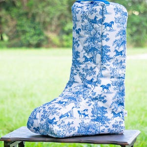 Puede incluir: Una funda para botas con estampado azul y blanco con un asa azul. El estampado presenta caballos y árboles.