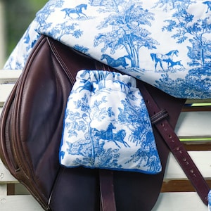 May include: A brown leather saddle with a blue and white patterned saddle blanket and a matching blue and white patterned saddle bag.