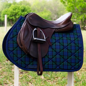 May include: A brown leather saddle with a silver stirrup, sitting on a blue and green plaid quilted saddle pad.