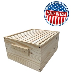 May include: A wooden beehive box with a slatted top and a handle on the side. The box is made of light-colored wood and has a "MADE IN USA" sticker in the upper right corner.