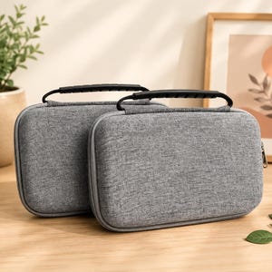 May include: Two rectangular, heather gray storage cases with rounded corners and a textured fabric exterior. Each case features a black plastic carrying handle attached to the top and a metal zipper closure running along the perimeter of the case.
