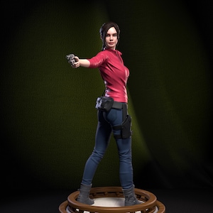 Könnte beinhalten: Detaillierte Figur einer Frau in rotem Oberteil und blauer Hose, die eine Pistole hält. Die Figur steht auf einer braunen, mehrstufigen Plattform. Die Figur hat einen schwarzen Gürtel mit Taschen und trägt graue Stiefel. Der Hintergrund ist strukturiertes Grün.
