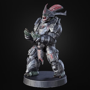 May include: A detailed figurine of a character in dark armor with red accents, posed on a circular base. The figure has a green face with sharp teeth and is holding its hands up. The armor has intricate details and a helmet with horns.