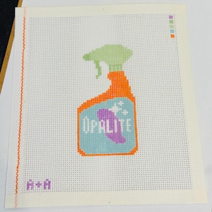 Könnte beinhalten: Nadelmalerei-Leinwand mit einem Sprühflaschendesign. Die Flasche ist orange mit einer hellgrünen Sprühdüse und einem hellblauen Etikett mit dem Wort "OPALITE" und einem lila Design. Die Leinwand hat einen weißen Hintergrund.