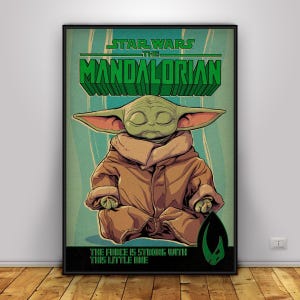 May include: A framed poster featuring Grogu from The Mandalorian. The poster has a teal and green background with the words "Star Wars The Mandalorian" in green 3D lettering. The text "The Force is Strong With This Little One" is at the bottom.