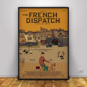 May include: A framed movie poster for "The French Dispatch" with a vintage aesthetic. The poster features a detailed illustration of a city scene, a cyclist, and the film's title in bold letters. The poster includes the text "The Cycling Reporter" and the name "Owen Wilson".