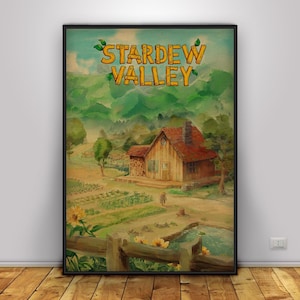 May include: A framed print featuring the text "Stardew Valley" above a watercolor painting of a rural landscape. The artwork depicts a wooden house with a red roof, a garden, and a pond, all set against a backdrop of green hills.