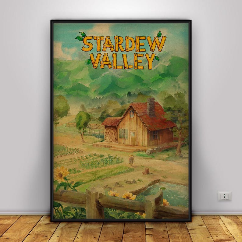 May include: A framed print featuring the text "Stardew Valley" above a watercolor painting of a rural landscape. The artwork depicts a wooden house with a red roof, a garden, and a pond, all set against a backdrop of green hills.