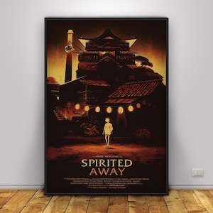 Op de afbeelding: Een ingelijste poster met de animatiefilm "Spirited Away". De afbeelding toont een jong meisje op een pad, met een traditioneel Japans gebouw op de achtergrond. De poster heeft een donker, warm kleurenpalet met de titel van de film.